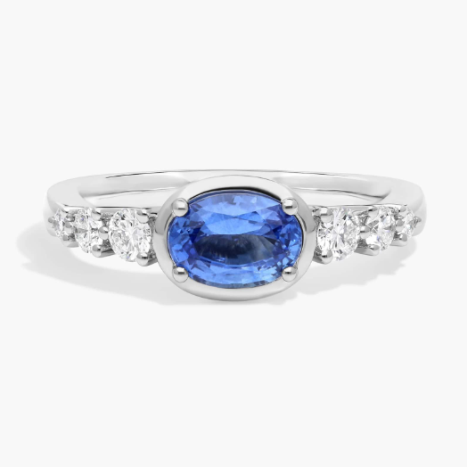 East-West Oval Cut Sapphire Ring With Half Bezel and Diamond Accent In 14K White Gol